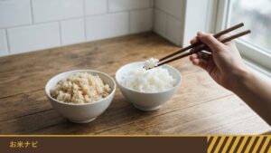 茶碗に盛った玄米ご飯と白米のご飯が並び、色の違いが分かる食卓で、箸でご飯をつまもうとしている手元