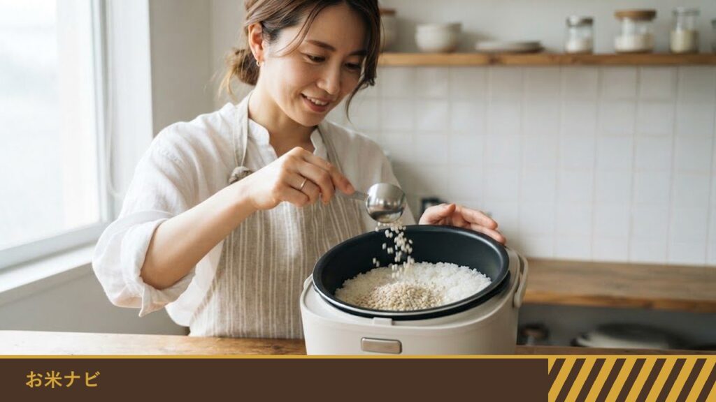 台所で、女性が炊飯器の内釜の白米に、計量スプーンでもち麦を加えている様子